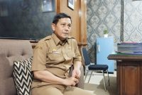 SANTAI: Kepala Dinsos P3A Sumenep, Mustangin, saat diwawancarai tentang program sekolah gratis di ruangannya (SandiGT - Seputar Jatim)