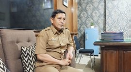 SANTAI: Kepala Dinsos P3A Sumenep, Mustangin, saat diwawancarai tentang program sekolah gratis di ruangannya (SandiGT - Seputar Jatim)