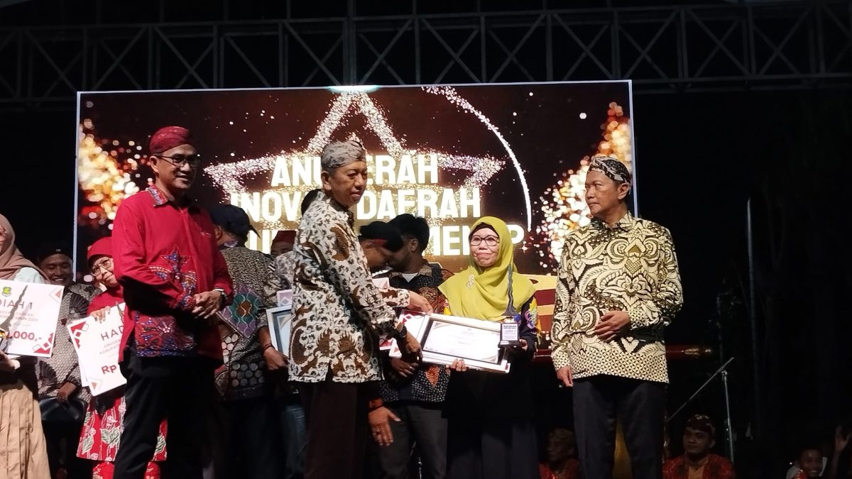 SERAH TERIMA: Kepala Bidang Pelayanan Pendaftaran Penduduk Disdukcapil Sumenep, Wahasah, saat menerima penghargaan inovasi daerah 2025, yang diberikan oleh Plt Sekda R. Achmad Syahwan Effendy (SandiGT - Seputar Jatim)